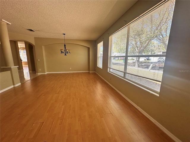 unfurnished dining area with a textured ceiling, arched walkways, light wood finished floors, and a chandelier