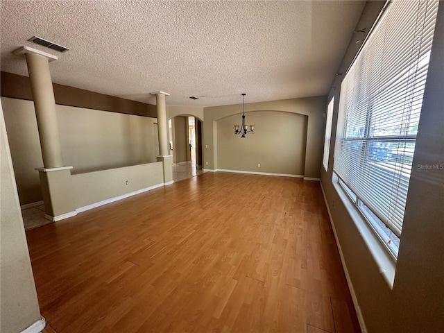 empty room with arched walkways, a notable chandelier, wood finished floors, and ornate columns