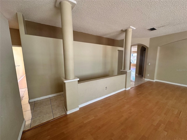 unfurnished room featuring arched walkways, a textured ceiling, ornate columns, and wood finished floors