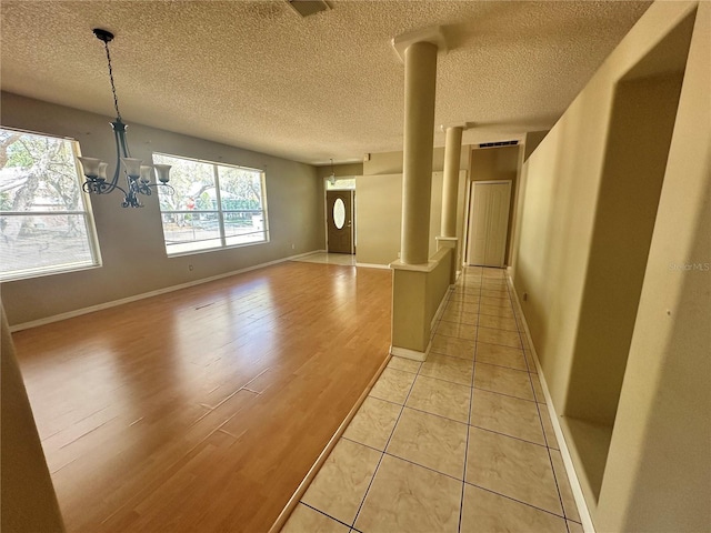 hall featuring baseboards, a chandelier, decorative columns, light wood-style flooring, and a textured ceiling