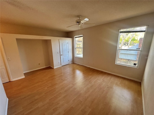 unfurnished bedroom with light wood-style flooring, a textured ceiling, baseboards, and a ceiling fan