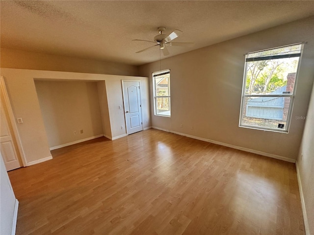 unfurnished bedroom with light wood-style flooring, a ceiling fan, baseboards, and a textured ceiling