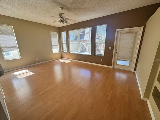 interior space featuring a textured ceiling, a ceiling fan, light wood-type flooring, and baseboards