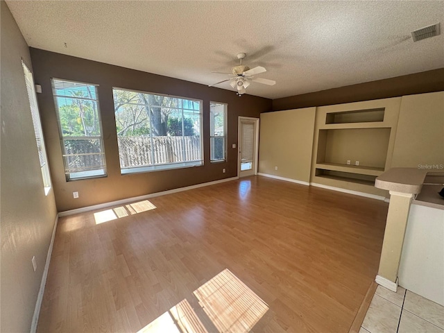 unfurnished living room featuring visible vents, a textured ceiling, light wood-type flooring, and ceiling fan