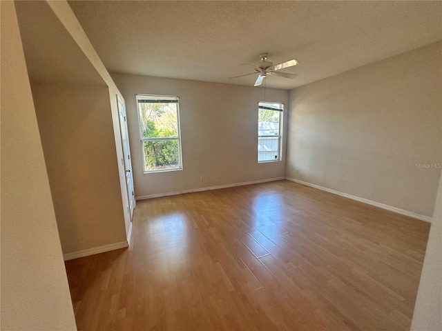 empty room with a textured ceiling, wood finished floors, baseboards, and ceiling fan