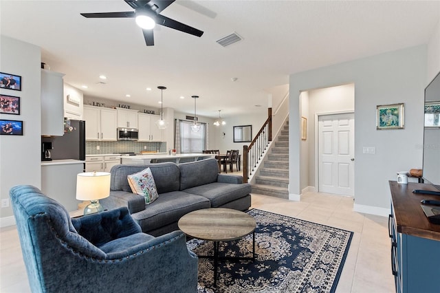 living room featuring visible vents, a ceiling fan, light tile patterned flooring, baseboards, and stairs