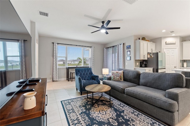 living area featuring light tile patterned floors, visible vents, baseboards, and ceiling fan