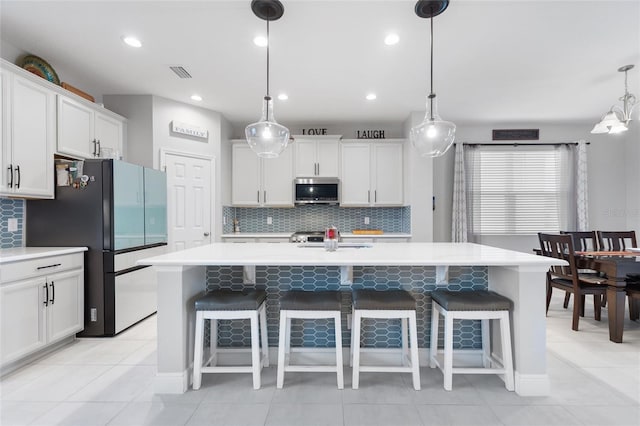 kitchen with visible vents, stainless steel microwave, freestanding refrigerator, white cabinets, and light countertops