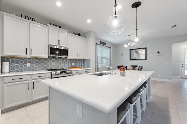 kitchen featuring a kitchen island with sink, a sink, backsplash, stainless steel appliances, and light tile patterned floors