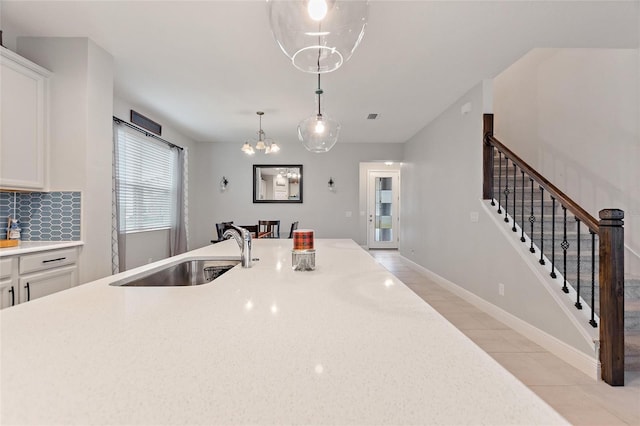 kitchen with a sink, tasteful backsplash, white cabinetry, light countertops, and hanging light fixtures