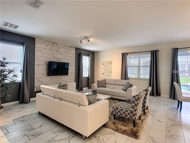 living room with an accent wall, visible vents, and marble finish floor