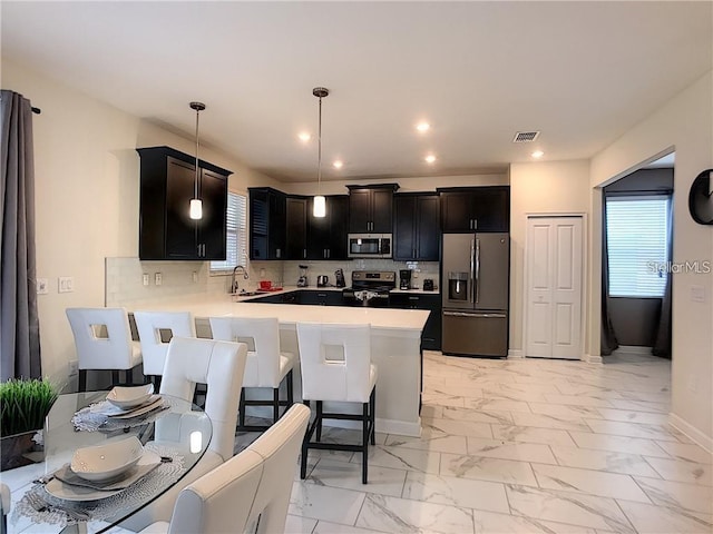 kitchen featuring backsplash, marble finish floor, a peninsula, and stainless steel appliances