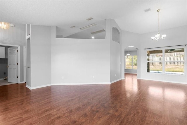 unfurnished living room featuring wood finished floors, arched walkways, a high ceiling, baseboards, and a chandelier