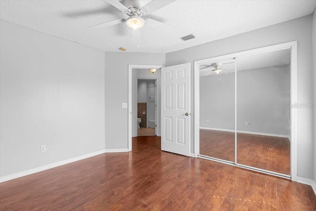 unfurnished bedroom with visible vents, a textured ceiling, a closet, and wood finished floors