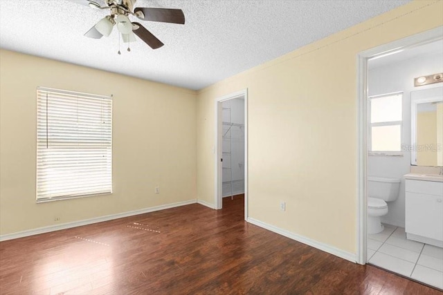 unfurnished bedroom featuring wood finished floors, baseboards, a textured ceiling, a walk in closet, and connected bathroom