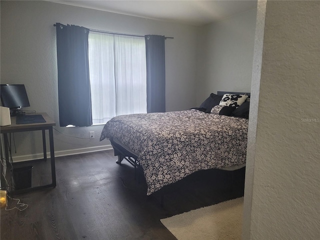 bedroom with wood finished floors, a textured wall, and baseboards