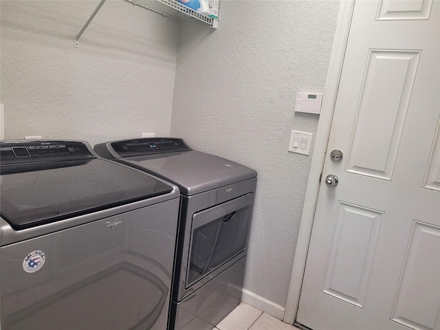 clothes washing area featuring light tile patterned flooring, washing machine and dryer, laundry area, baseboards, and a textured wall