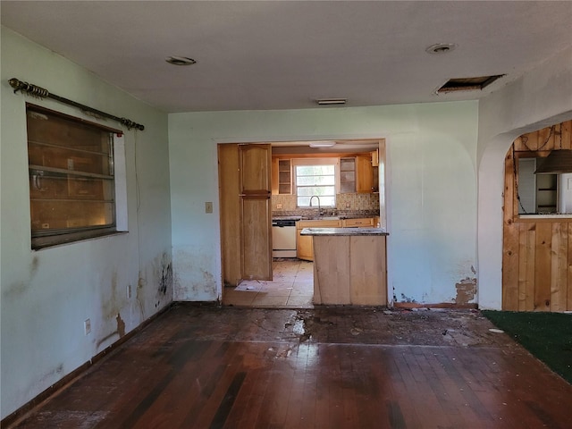 kitchen featuring hardwood / wood-style floors, dishwashing machine, arched walkways, brown cabinets, and backsplash