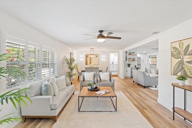 living room featuring light wood-style flooring, baseboards, visible vents, and ceiling fan