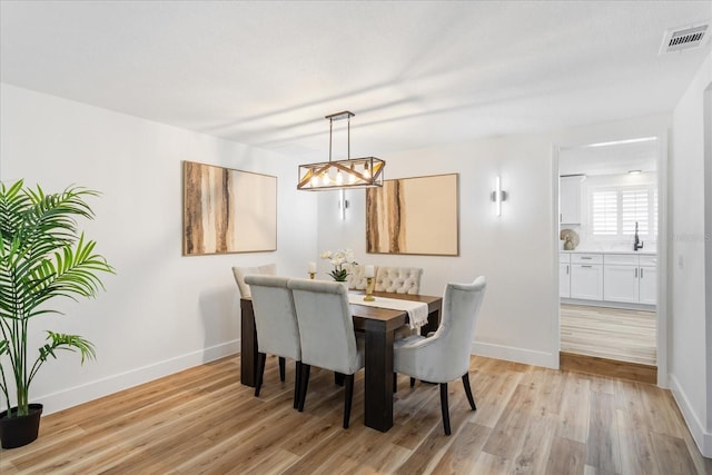 dining space featuring light wood finished floors, visible vents, a notable chandelier, and baseboards