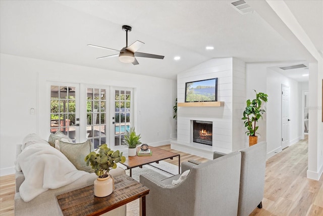 living room with a ceiling fan, visible vents, light wood finished floors, lofted ceiling, and a fireplace