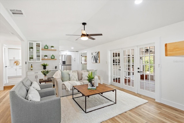 living room with visible vents, baseboards, vaulted ceiling, light wood-style flooring, and a ceiling fan