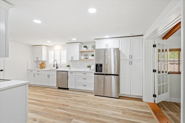 kitchen with light wood finished floors, tasteful backsplash, white cabinetry, stainless steel appliances, and light countertops