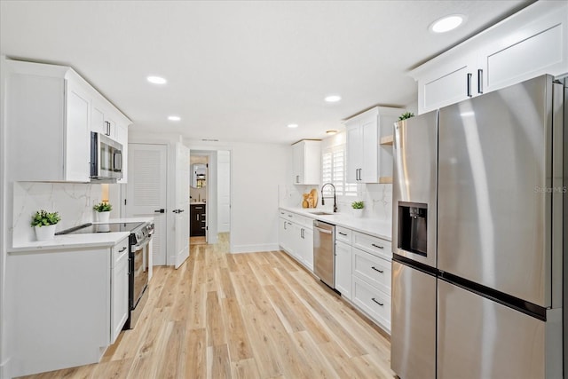 kitchen featuring light wood-style flooring, a sink, tasteful backsplash, white cabinetry, and appliances with stainless steel finishes