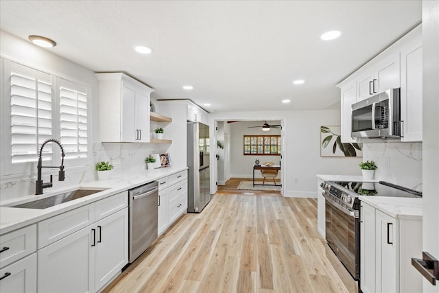 kitchen featuring open shelves, light wood-style flooring, a sink, white cabinets, and appliances with stainless steel finishes