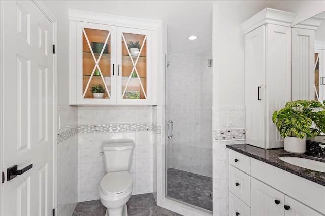 bathroom with vanity, a shower stall, toilet, and tile walls