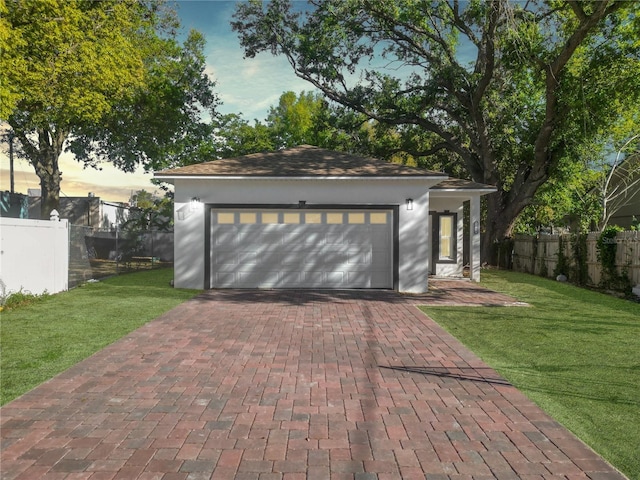 garage at dusk featuring a lawn and fence