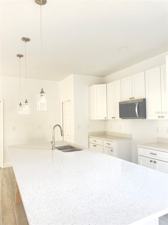 kitchen featuring a sink, stainless steel microwave, a spacious island, white cabinetry, and light stone countertops