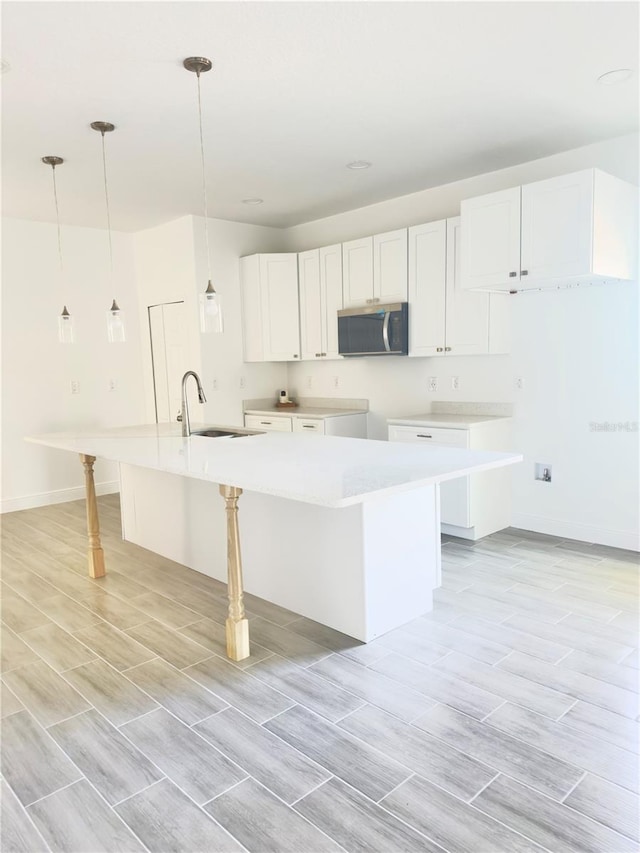 kitchen featuring wood finish floors, a sink, stainless steel microwave, decorative light fixtures, and white cabinetry