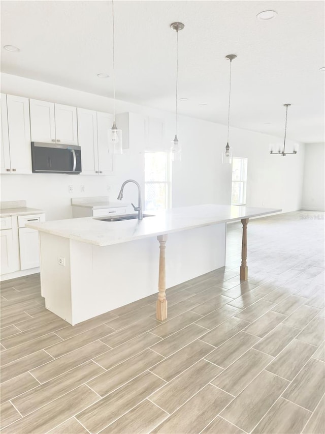 kitchen with a kitchen bar, a sink, stainless steel microwave, white cabinets, and hanging light fixtures