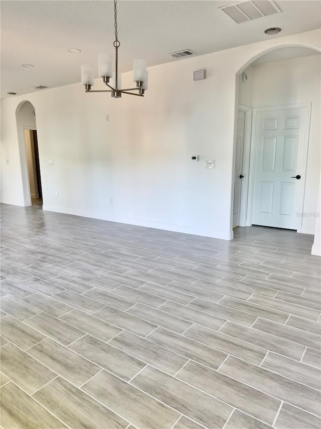 unfurnished room with an inviting chandelier, arched walkways, and visible vents