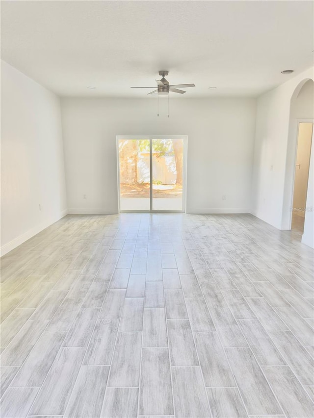 unfurnished room with baseboards, arched walkways, and a ceiling fan