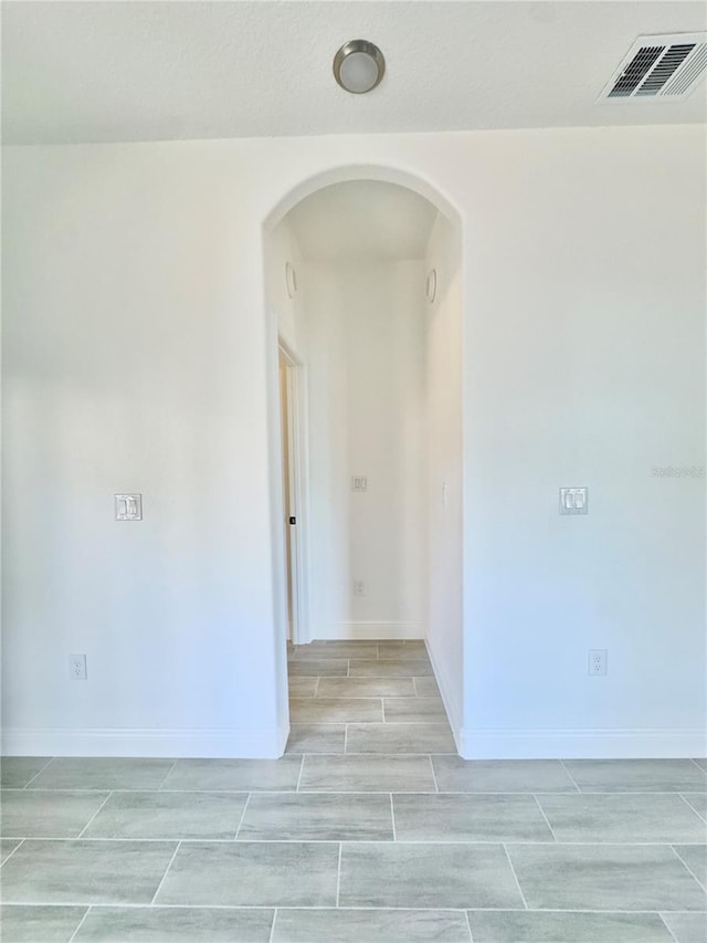 empty room with wood tiled floor, arched walkways, visible vents, and baseboards