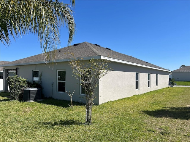 rear view of property featuring central air condition unit, stucco siding, and a lawn