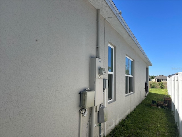 view of side of home with stucco siding, a yard, and fence