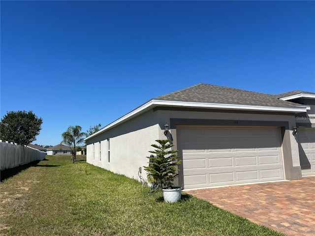 view of property exterior with fence, stucco siding, a garage, decorative driveway, and a lawn