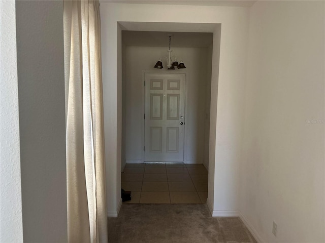 corridor featuring tile patterned floors, baseboards, a notable chandelier, and carpet