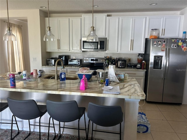 kitchen with light countertops, stainless steel appliances, light tile patterned flooring, white cabinetry, and a sink