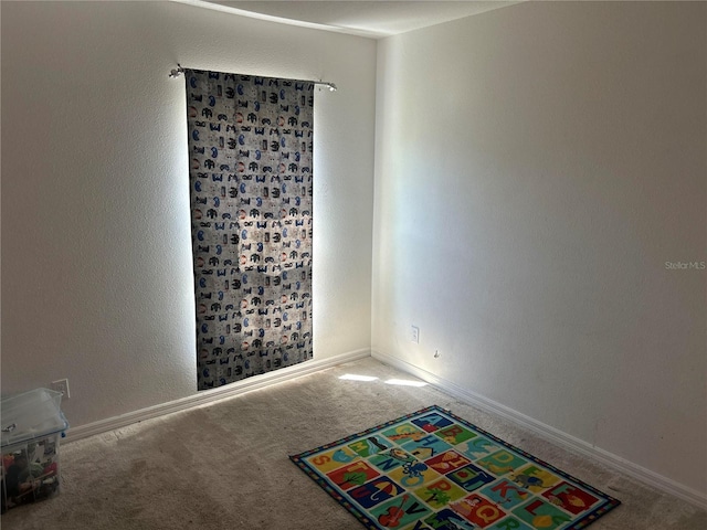 carpeted spare room with a textured wall and baseboards