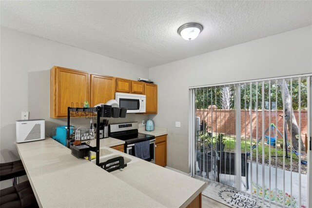 kitchen featuring white microwave, stainless steel electric stove, brown cabinetry, and light countertops