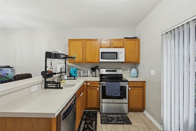 kitchen with brown cabinetry, light wood finished floors, a sink, stainless steel appliances, and light countertops