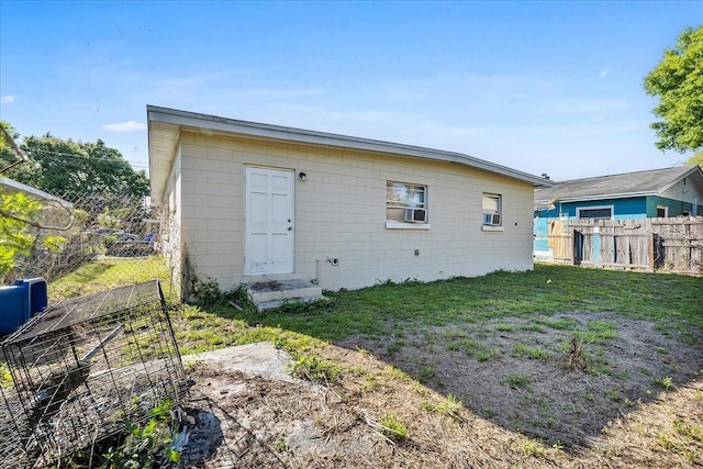 back of property with concrete block siding, a yard, fence, and cooling unit