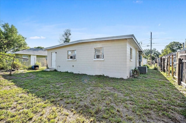 back of property with central air condition unit, a lawn, fence, cooling unit, and concrete block siding