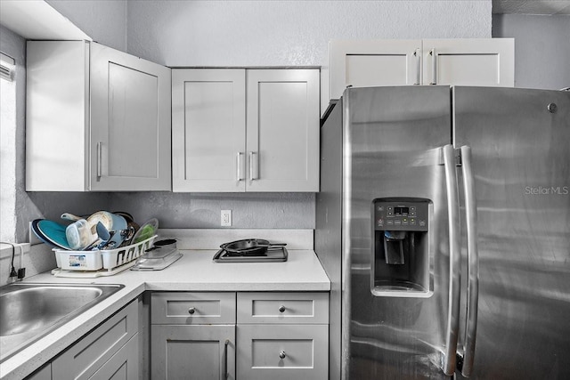 kitchen with gray cabinetry, stainless steel refrigerator with ice dispenser, a sink, light countertops, and a textured wall