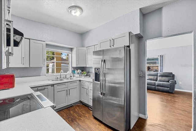 kitchen featuring dark wood finished floors, a sink, light countertops, a textured wall, and stainless steel fridge