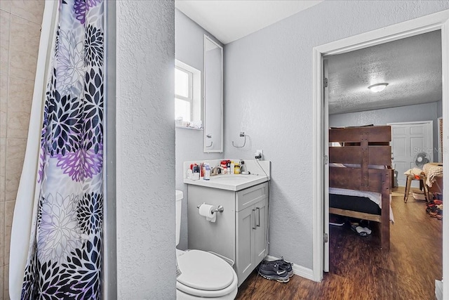 ensuite bathroom featuring vanity, wood finished floors, baseboards, and a textured wall